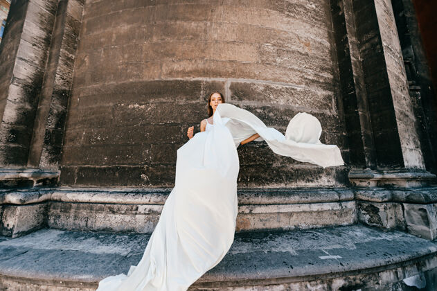 中世纪穿着白色飘逸长裙的年轻优雅女孩在古老的石墙上摆姿势女孩石头古代