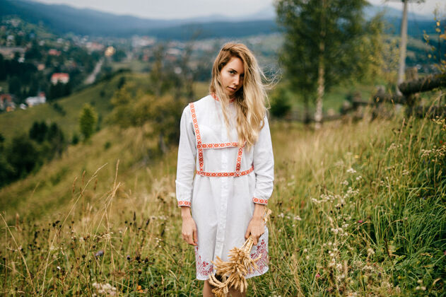女孩年轻迷人的金发女孩 穿着白色连衣裙 戴着小穗花束在风景如画的乡村风景中摆姿势风景金发乡村