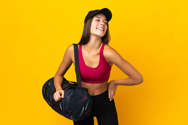肖像带着运动包的运动女人摆出双臂放在臀部微笑的姿势帽子健身运动