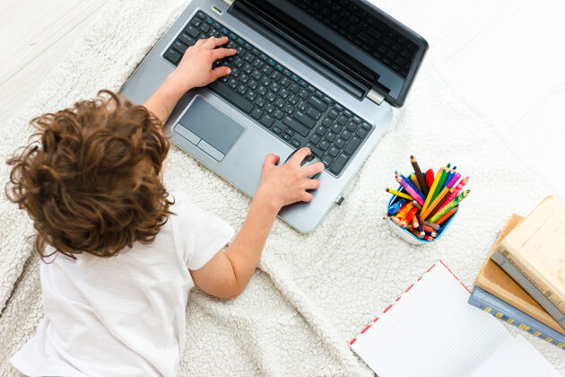 笔记本电脑卷发男孩看着监视器顶视图培训的概念 远程教育在第19期键盘工作场所视图