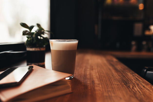 电话一杯咖啡 一本笔记本 一部手机在咖啡厅的桌子上马克杯奶油杯子