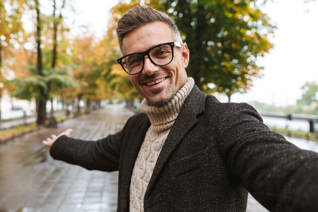 林荫大道30多岁的快乐男人穿着暖和的衣服微笑着 在户外穿过秋天的公园天气自拍阳刚