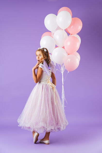 小一个穿着公主裙的漂亮小女孩孤零零地站在紫罗兰色的墙上 手里拿着一堆气球束童年爱