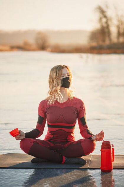 男人冬天 一个女孩在日落时在湖边的冰上做瑜伽热水瓶湖北方