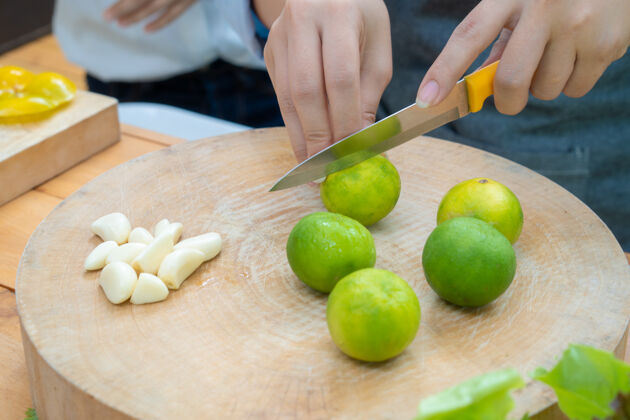 美味亚洲女性拿着橘子刀在旁边有花环的木制圆盘上滑动绿色柠檬酸橙盘子健康果汁