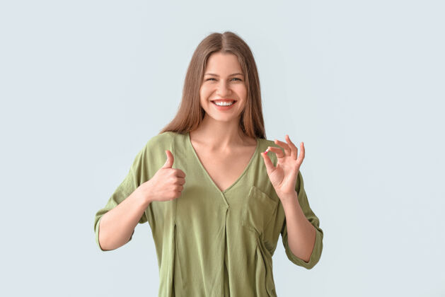 快乐美丽的年轻女子拿着药丸 在灰色的表面上摆出竖起大拇指的姿势食物症状病人