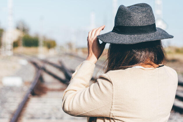 经典一个穿着米色雨衣戴着帽子的女人在废弃的铁轨上的后视图帽子延迟通勤