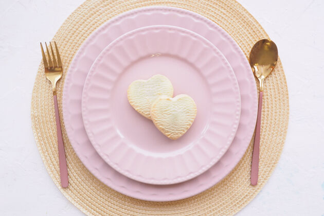 浪漫表格设置两个空的粉红色盘子 两个心形饼干 一把勺子和一把叉子放在一张白色的桌子上叉子盘子勺子