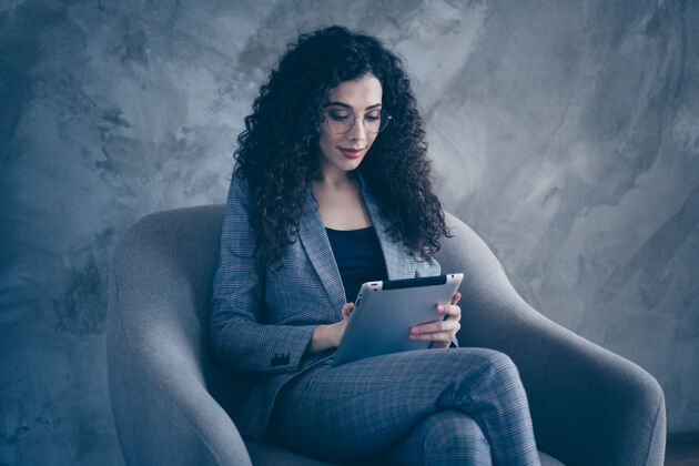 商务女性一头波浪形头发的经理女孩坐在椅子上阅读平板电脑隔离灰色背景的照片西装平板电脑使用