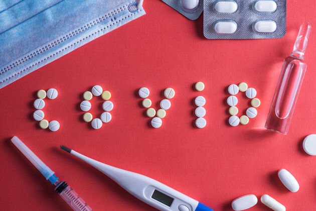 片剂铭文“covid” 由白色圆形一次性药片注射器和小瓶上的药物呈红色背景.covid-19冠状病毒疫苗空间为文本安瓿字母胶囊