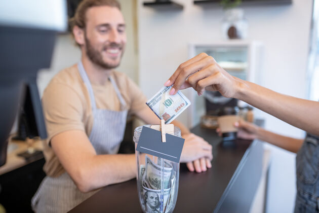 钞票支付订单.女士一只手伸出百元钞票买咖啡 柜台后面围着一个微笑的男人创业付款咖啡机
