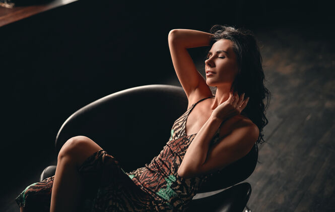 年轻一个漂亮的黑发女人的肖像 穿着一件裙子 坐在扶手椅上摆姿势 用手拉直她的长卷发惊艳性感女人