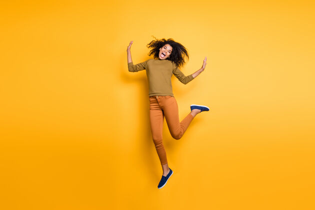 跳投全身尺寸的卷曲波浪的照片相当甜蜜兴奋疯狂的女孩穿着橙色裤子裤子鞋绿色speater隔离黄色生动的色彩背景黑发皮肤幸运
