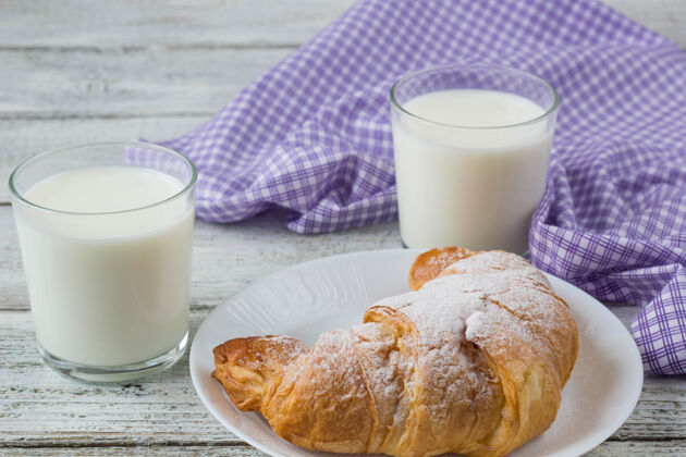 健康羊角面包和牛奶放在旧木桌上作为早餐的背景牛奶早餐杯子