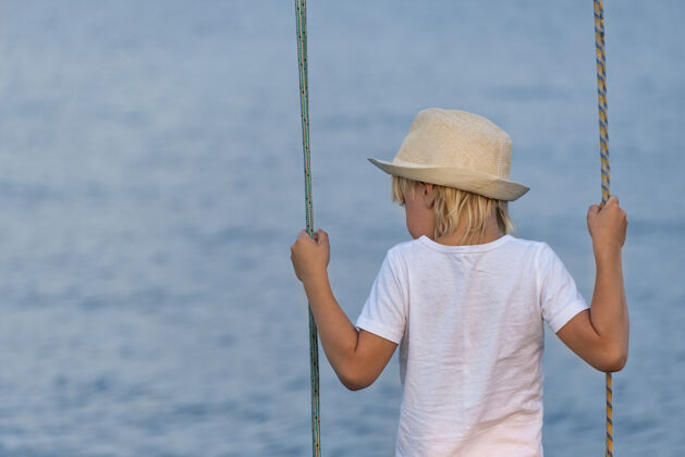 秋千戴草帽的男孩骑在秋千上俯瞰着天空海快乐童年青年热带乐趣