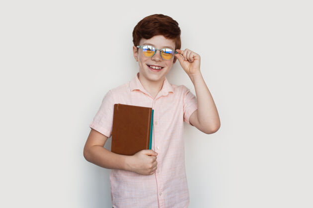 拥抱一个戴眼镜的白人姜男孩穿着休闲服 拿着一些书对着镜头微笑小学生休闲小学生