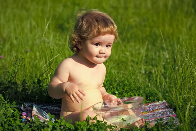 爱小宝宝坐在绿草上 拿着玻璃盘子自然收获肖像