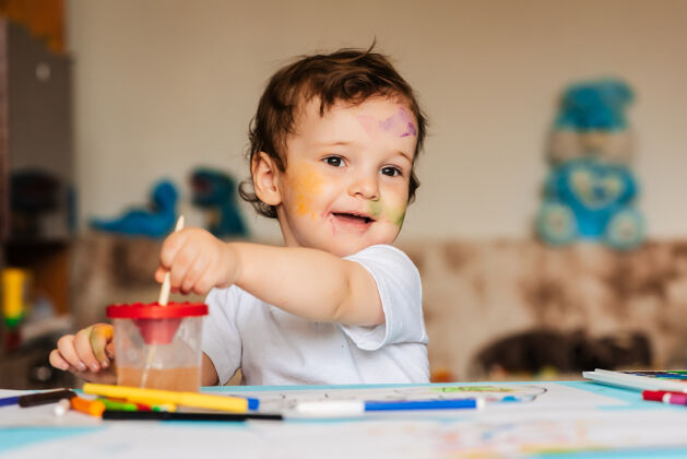 蜡笔一个可爱的小男孩用画笔和彩色颜料在一张纸上画画画笔童年幼儿园