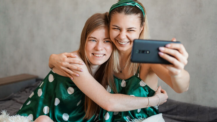小玩意两个美丽快乐的女朋友在睡衣派对上用智能手机拥抱自拍团体漂亮生活方式