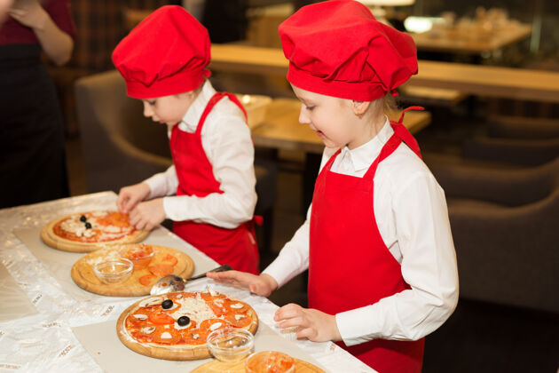 厨房两个穿着白衬衫和红围裙的漂亮厨师女孩在餐厅做比萨饼准备厨师食物
