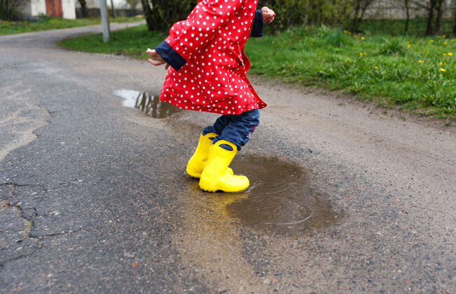 水坑一个穿着黄色靴子的小女孩跳到了春天的水坑上 离水坑很近-起来开心童年靴子大自然孩子
