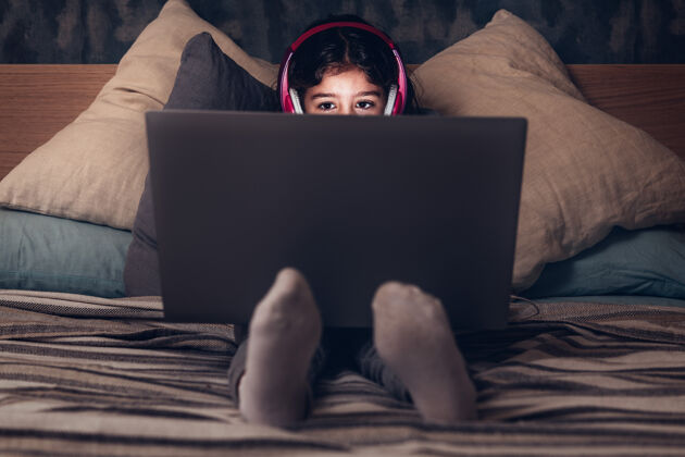 专注坐在床上拿着电脑的小女孩舒适耳机放松