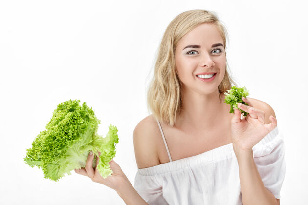 生菜一个穿着白衬衫的金发美女在白衬衫上吃着新鲜的蔬菜沙拉背景.健康还有节食自然成人蔬菜