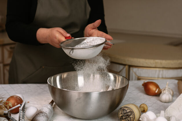 厨师穿着围裙的女厨师用金属筛面粉碗准备制作一个面团来烘烤或雕刻方便食品房子家庭主妇木材