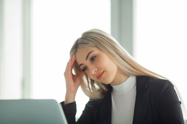 女性漂亮的年轻女子穿着西装在办公室的桌边拿着笔记本电脑经理白种人疲劳