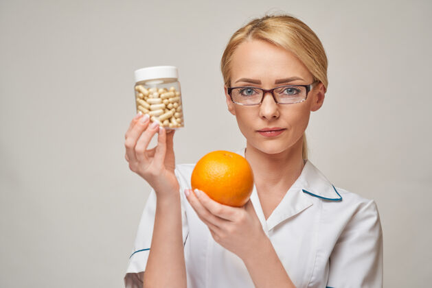 女性营养学家医生健康的生活方式概念-持有橘子水果和营养维生素胶囊或药丸健康饮食医生
