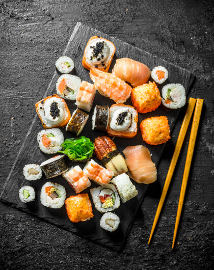 大米美味的面包卷 寿司和maki放在石头板上筷子.on黑色乡村背景晚餐鳄梨准备