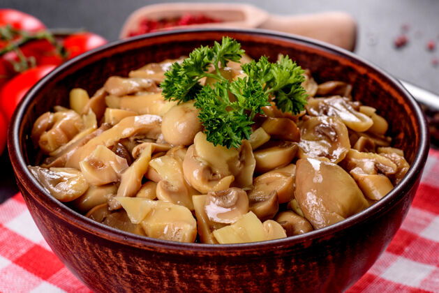 棕色新鲜美味的辛辣蘑菇罐头与香料和草药在陶瓷菜肴在黑暗的混凝土背景新鲜香菇木耳
