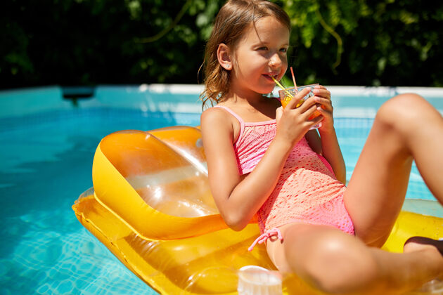 美丽小女孩在游泳池里放松 享受日光浴 在家庭度假时在水里的黄色充气床垫上喝果汁玩耍娱乐鸡尾酒