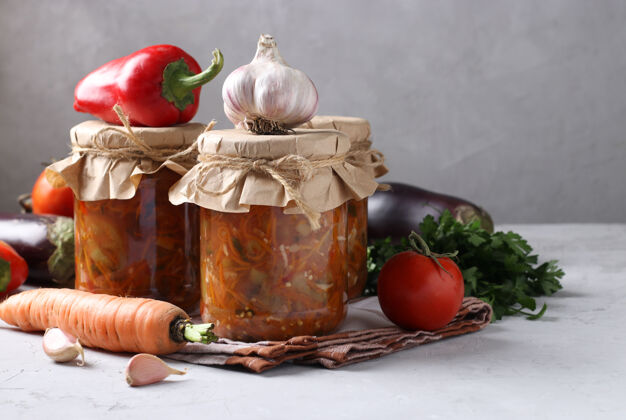 饮食蔬菜沙拉配茄子 胡萝卜 辣椒 大蒜和西红柿 放在灰色表面的玻璃罐中 水平排列醋茄子蔬菜