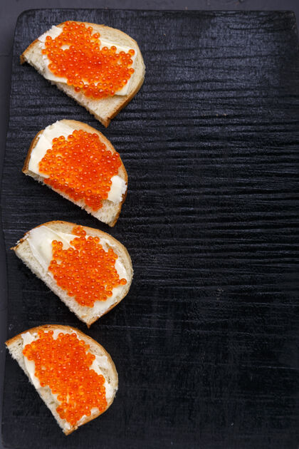 熟食涂有黄油和红色鱼子酱的布氏面包铺在灰色水泥表面的黑色木板上食物新鲜海洋