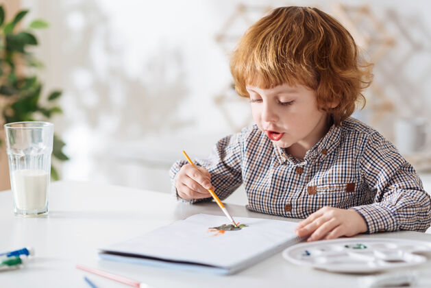 上午混合色彩 艺术漂亮的红头发的孩子坐在白色的桌子旁 用水彩画和他的想象力创造了奇异的画面自我儿童世代