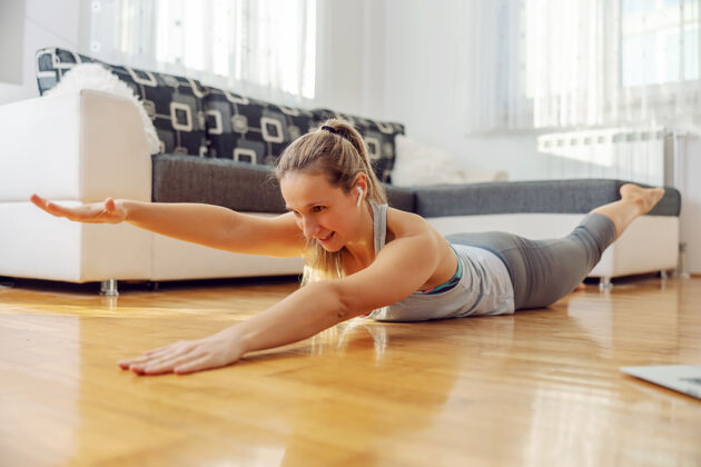 健康微笑的女运动员趴在地上做背部练习 在隔离期间跟随在线课程地板运动在线