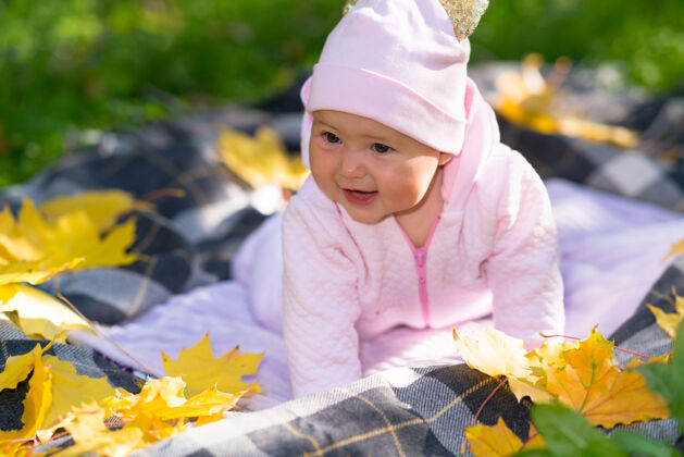 刺激可爱快乐的小女婴 穿着粉红色的衣服 在秋天的户外玩耍 躺在草地上的地毯上 周围是五颜六色的黄叶可爱欢呼小