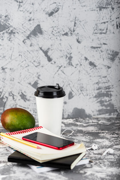 电脑工作或教育去吧咖啡杯子 芒果 红色的智能手机和一堆放在灰色石头上的记事本表.copy空间办公室工作场所桌子