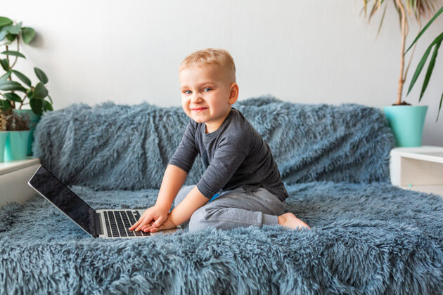 相机小男婴在家里的沙发上玩笔记本电脑电子学习 远程学习 远程交流的概念会议祖父母在线