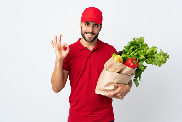 健康一个留着胡须的年轻人手里拿着一个装满蔬菜的袋子 在白色的背景上用手指显示一个ok标志胡须外卖新鲜