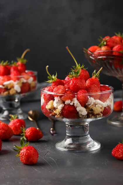 奶油甜点与草莓 干酪和饼干在玻璃酒杯反对黑暗的表面 垂直照片分散美味草莓