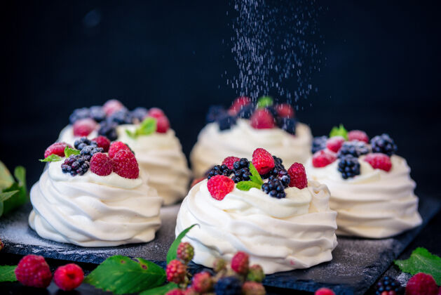 甜点巴甫洛娃蛋糕的自制蛋白酥皮 配以新鲜蓝莓 黑莓和糖粉 表面为黑色混凝土纹理自制美食美味