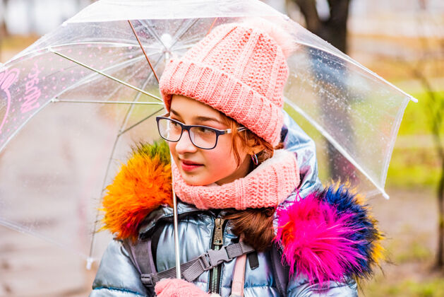 寒冷金发碧眼的女孩穿着夹克带着透明的雨伞在外面的雨中御寒夹克天气伞