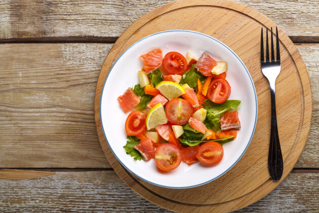 清淡的菜肴一盘三文鱼 樱桃西红柿沙拉和蔬菜沙拉放在一张木桌上 放在叉子旁边的木架上健康鱼片三文鱼