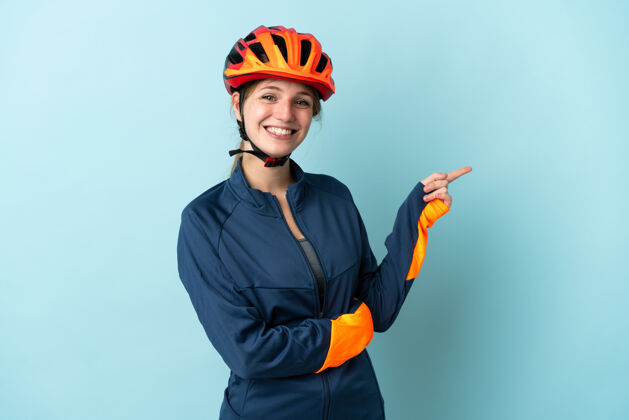 产品一个年轻的骑自行车的女人被隔离在蓝色的背景下 手指指向一边女孩自行车女性