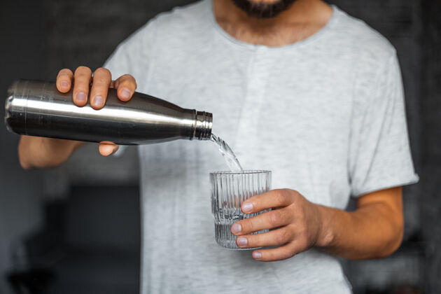 瓶子男性的手把水从热生态钢瓶倒进杯子里闪亮青少年健身