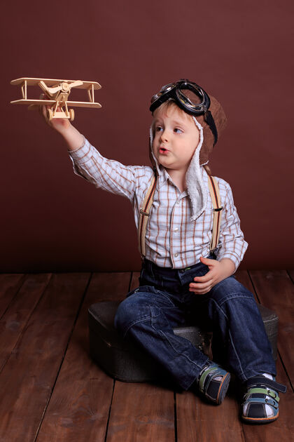白种人戴头盔的小男孩和木头玩具玩飞机男孩梦想成为一名教师飞行员假期男人们眼镜幼儿园游戏