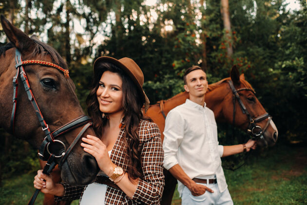动物一个戴帽子的怀孕女孩和一个穿白衣服的男人站在森林里的马旁边自然时尚孕妇带着丈夫带着马结婚了一对夫妇散步白布