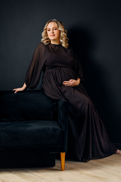 产前孕妇穿着优雅的黑色连衣裙在室内摄影棚摆姿势黑色墙壁背景金发白人中年女性怀孕6个月成人分娩孕妇
